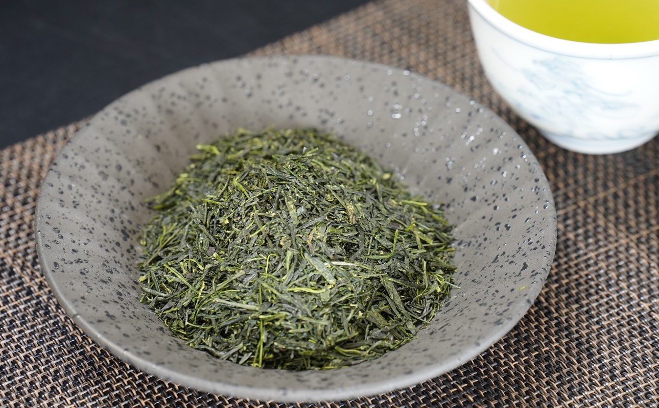 灰色の斑点の器に盛られた緑色の茶葉と湯のみ