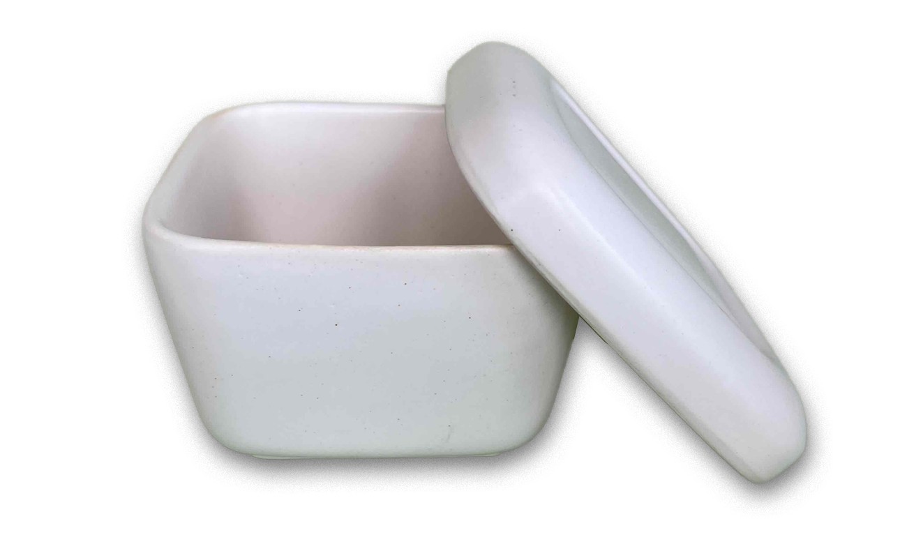蓋が斜めに外れて半開きになっており、内部も白く空になっている。艶のあるマットな質感で、弁当箱や保存容器のような形状。