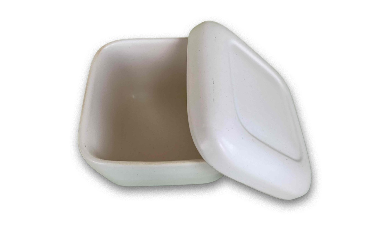 蓋が斜めに外れて半開きになっており、内部も白く空になっている。艶のあるマットな質感で、弁当箱や保存容器のような形状。