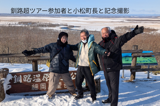 釧路湿原の雄大な景色をバックに、笑顔で記念撮影をする小松町長とツアー参加者の皆様。