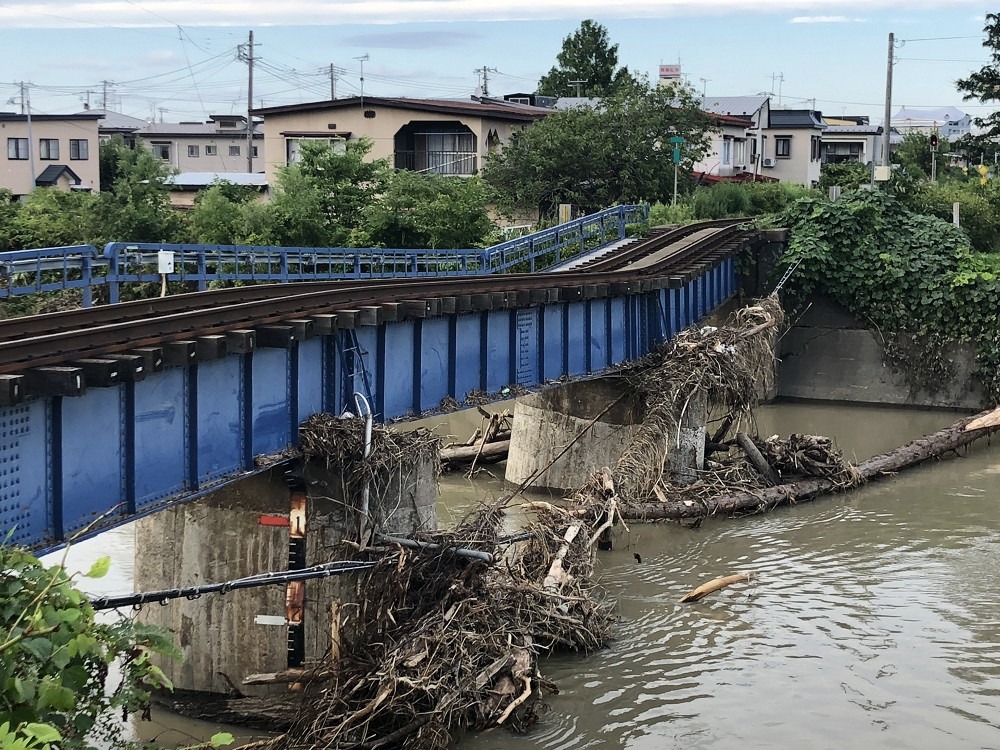 一夜明け、水位が下がった中村川橋脚には大きな流木が引っかかり、橋の一部は沈み込み線路は折れ曲がっています。