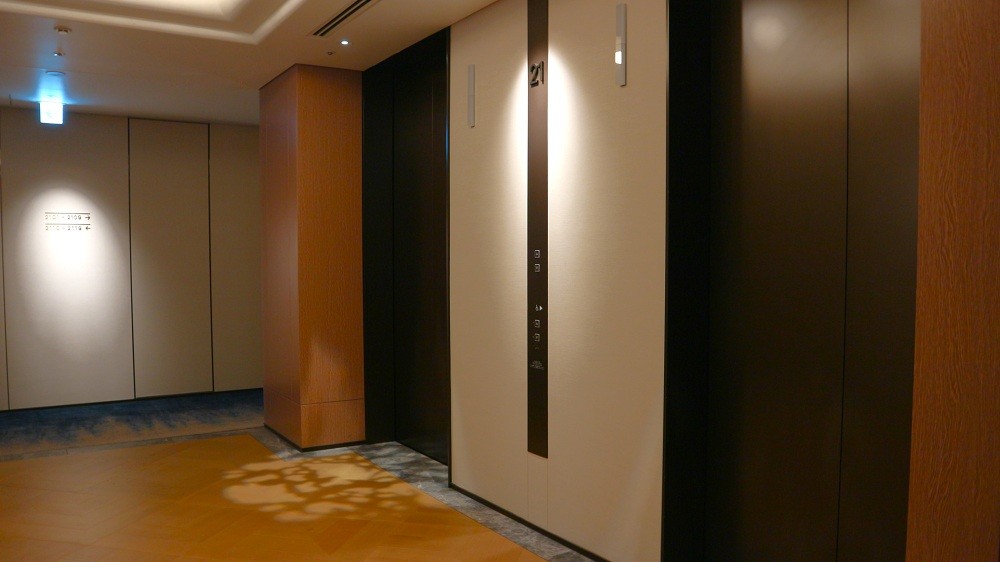 波をイメージした廊下と木漏れ日のダウンライトが光るエレベーターホール
